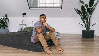 A man sits on a mattress on the floor before he falls asleep